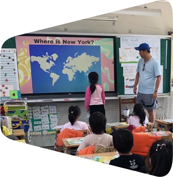 a man standing in front of a classroom full of children showing them where New York is on a map