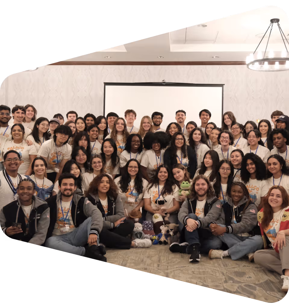 Large diverse group of smiling young adults wearing matching t-shirts, seated and standing together in a conference room.
